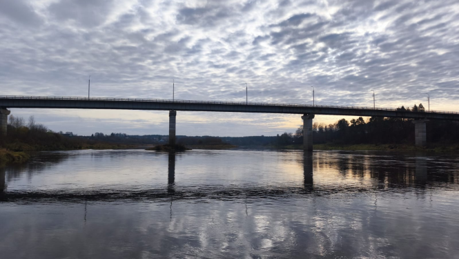 Foto redzams skats uz Daugavu, pāri upei iet tilts un paveras skats uz debesīm