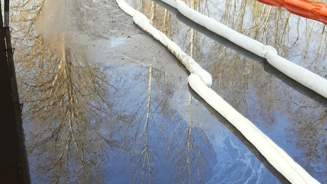 Naftas produktu absorbējošas bonas upē, kur redzams naftas produktu piesārņojums