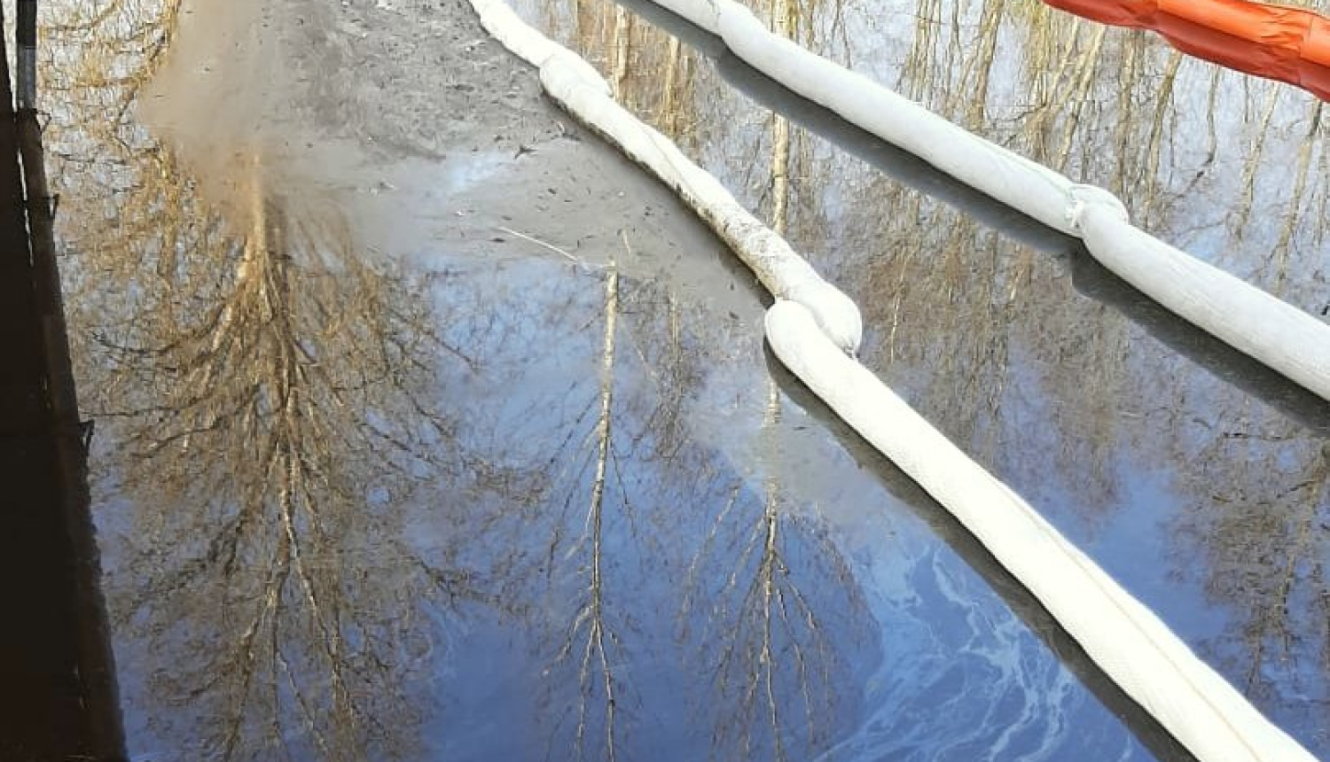Naftas produktu absorbējošas bonas upē, kur redzams naftas produktu piesārņojums